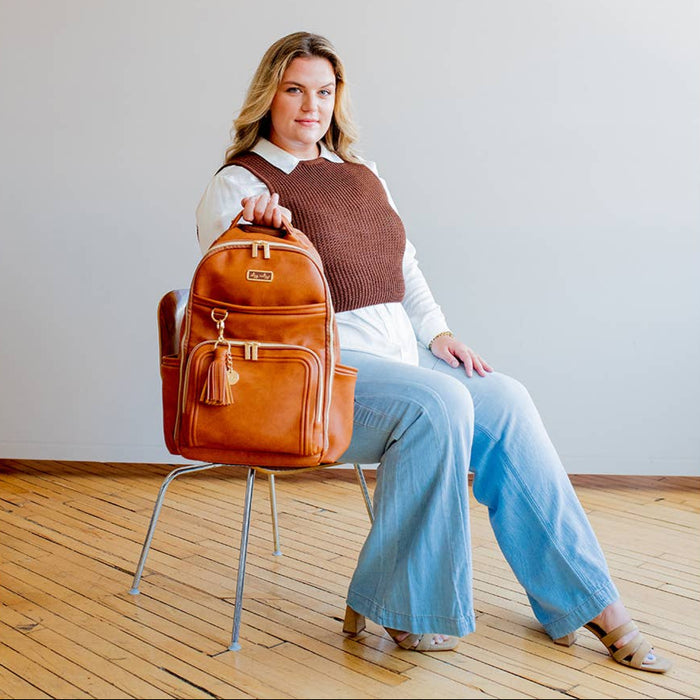 Woman holding a brown leather backpack in a minimal indoor setting